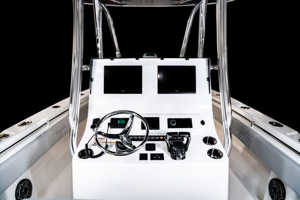 A modern boat control console featuring a steering wheel, dual display screens, various switches, and controls, mounted on a white surface with stainless steel railings.