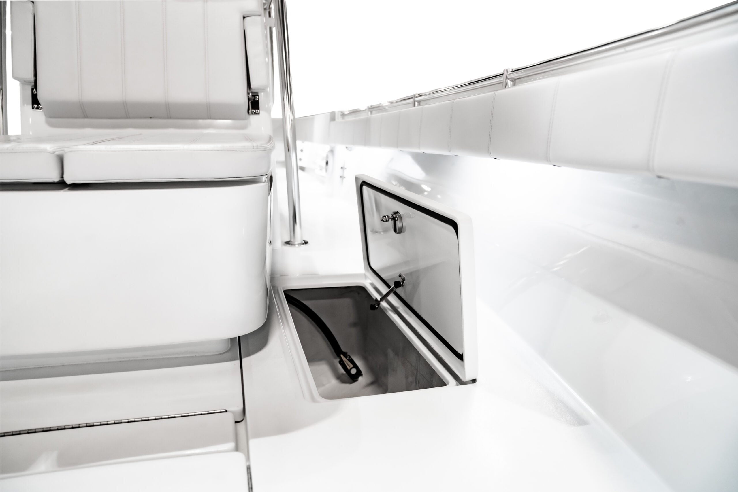 Close-up of a white boat interior showing a storage compartment with an open hatch. A hose is partially visible inside the compartment.