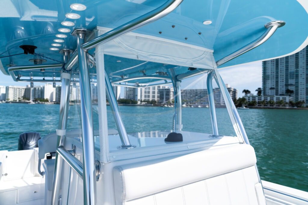 View of a boat's seating area with metal framework and partial canopy, set against a backdrop of a waterfront cityscape with high-rise buildings and green water.