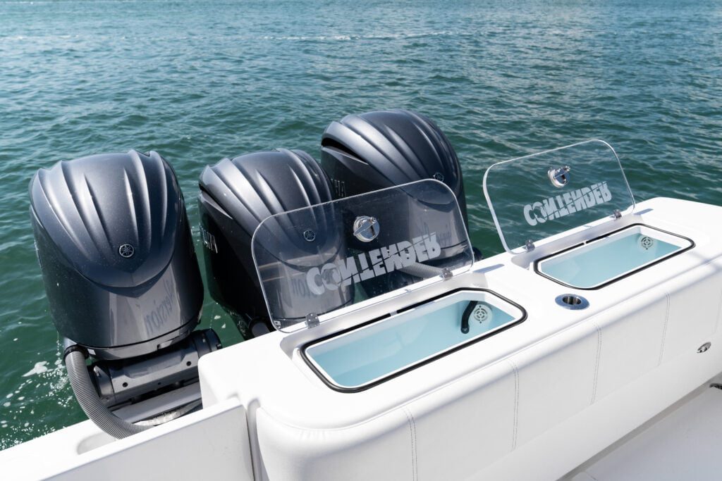 A white boat with four outboard engines, two transparent bait wells with blue water, and clean white cushioning on a sunny day out on the water.