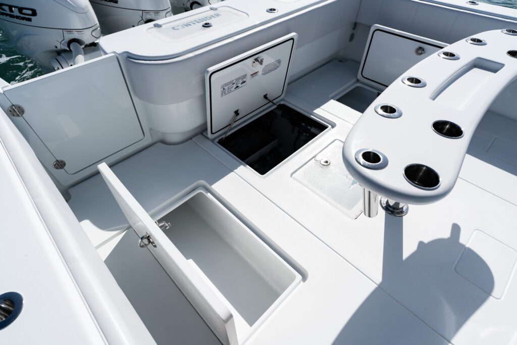 The image shows the deck of a boat, equipped with open storage compartments and hatches. Multiple cup holders are integrated into the structure. The motor engine area is partially visible.