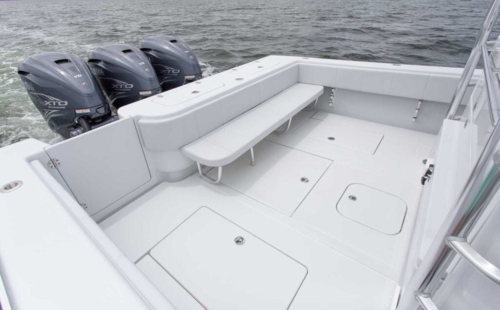 The image shows the rear deck of a boat equipped with three outboard motors and a bench seating area. The boat is on water.