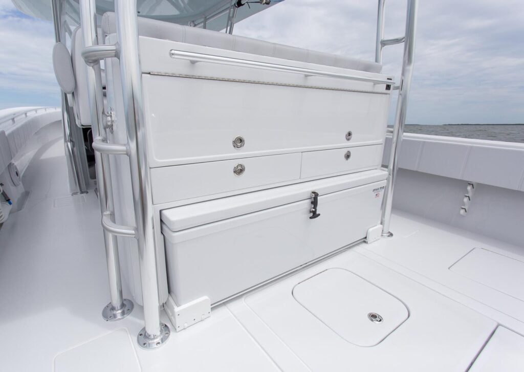 A close-up view of storage compartments, including drawers and a locking box, on the deck of a white boat with a cloudy sky in the background.