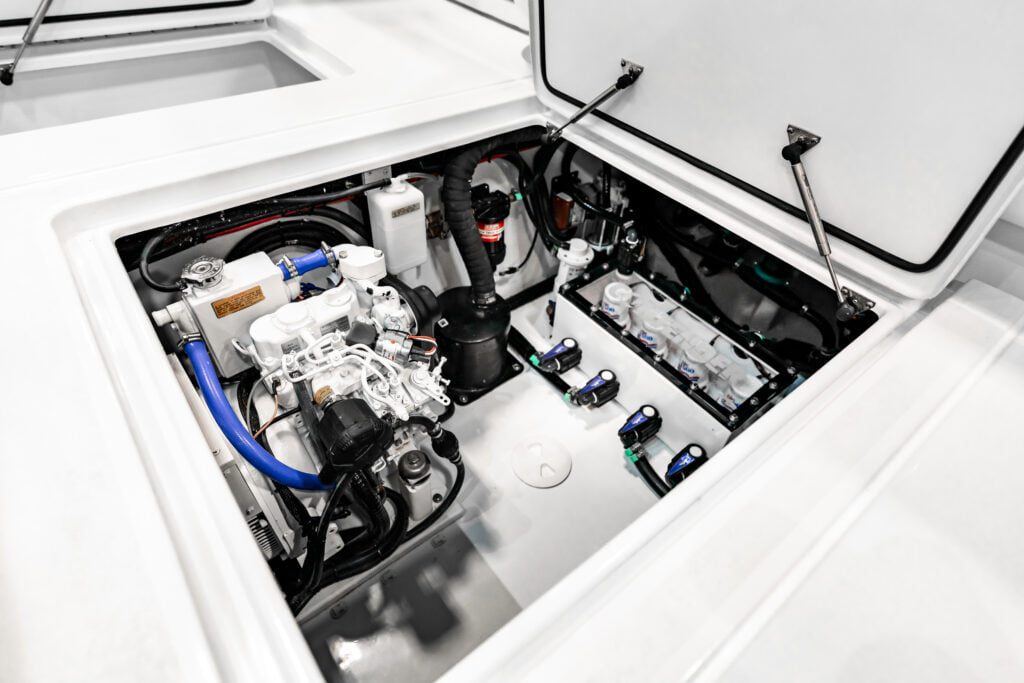 View of an open engine compartment in a boat, showing various mechanical and electrical components, including wiring, hoses, and connectors against a white interior background.
