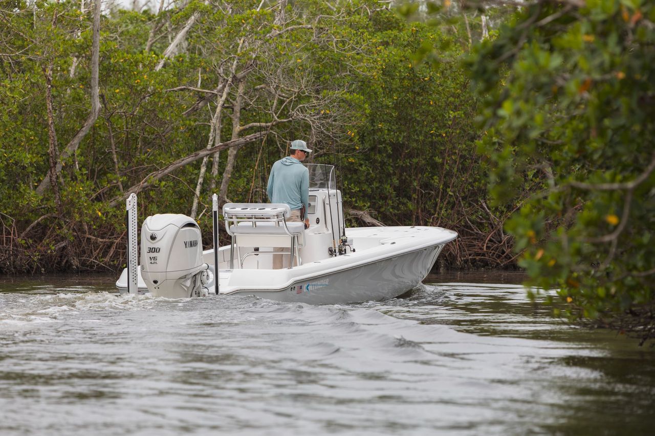 A person is steering a small white motorboat in a narrow waterway surrounded by dense green vegetation.