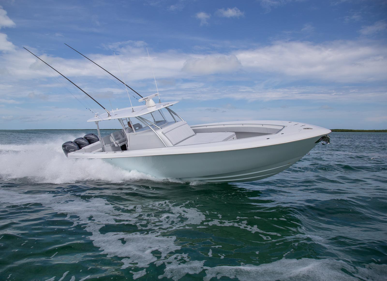 A white motorboat with two fishing rods speeds across open water under a partly cloudy sky.