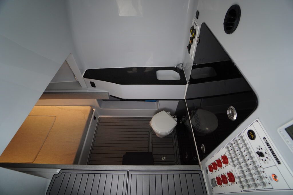Image of a small, modern bathroom with a toilet, a built-in bench, and a control panel with buttons and switches.
