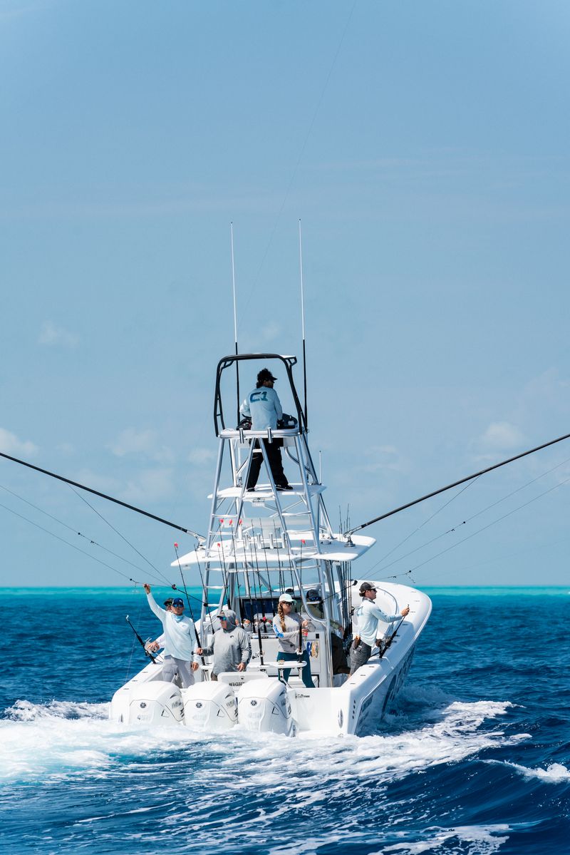 A group of people fishing on a white boat in open blue waters under a clear sky.