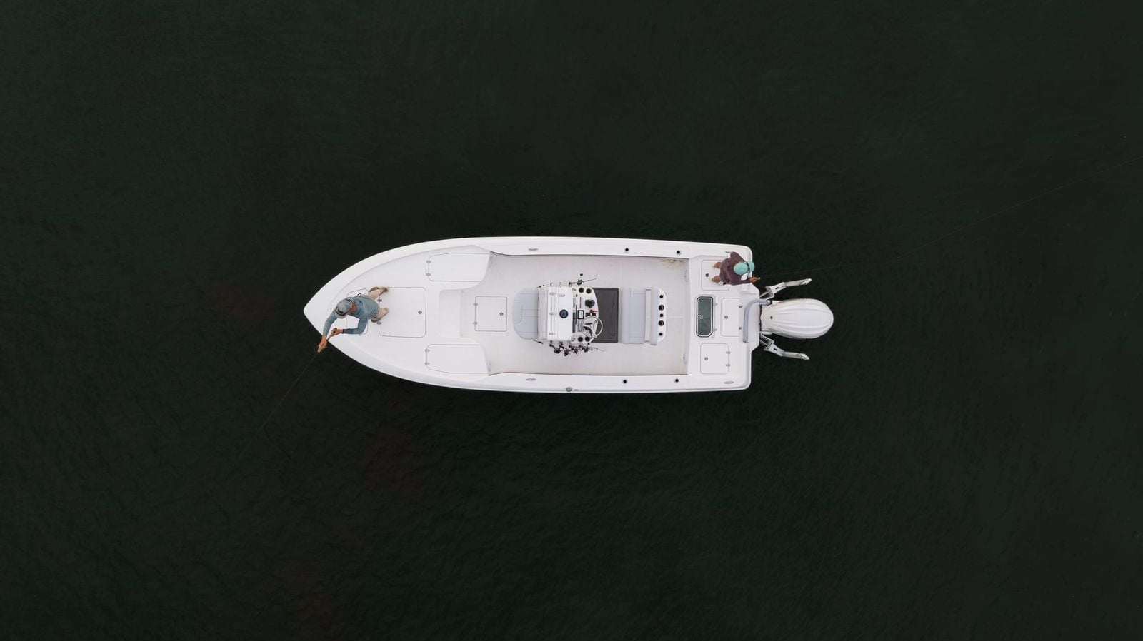 Top view of a white boat with two people fishing on either side in dark, calm waters.