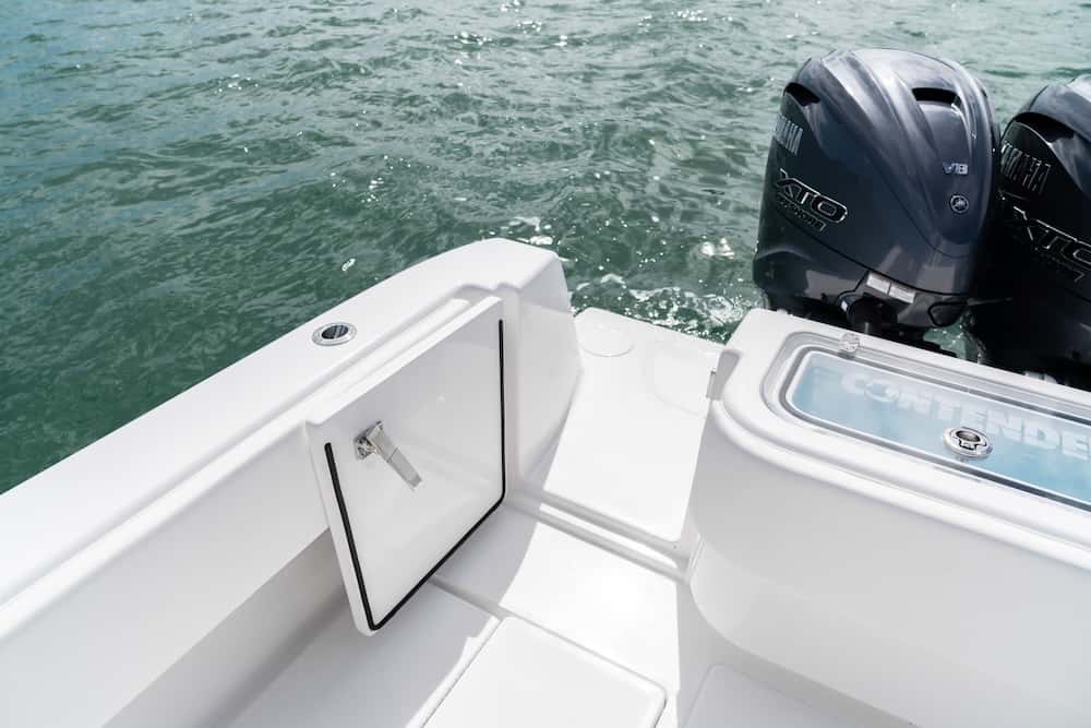 A white boat on water with two outboard motors and an open storage compartment on the deck.
