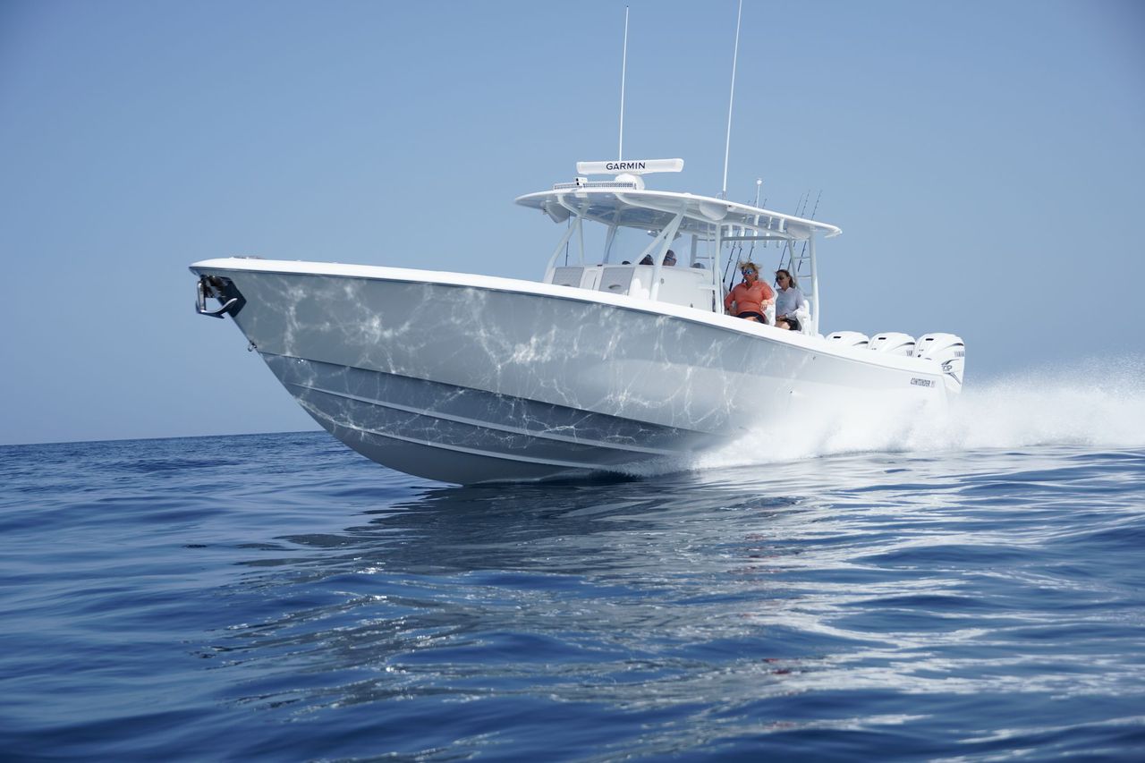 A white motorboat speeds across a calm body of water under a clear sky, creating a splash at the bow.