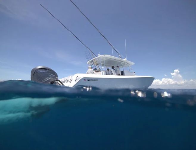 A white motorboat with fishing rods is partially submerged in the blue ocean. The sky is clear with a few clouds.