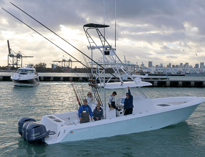 A boat with four people on board is docked near a harbor. Fishing rods are visible on the boat, and cranes and a cityscape are in the background.