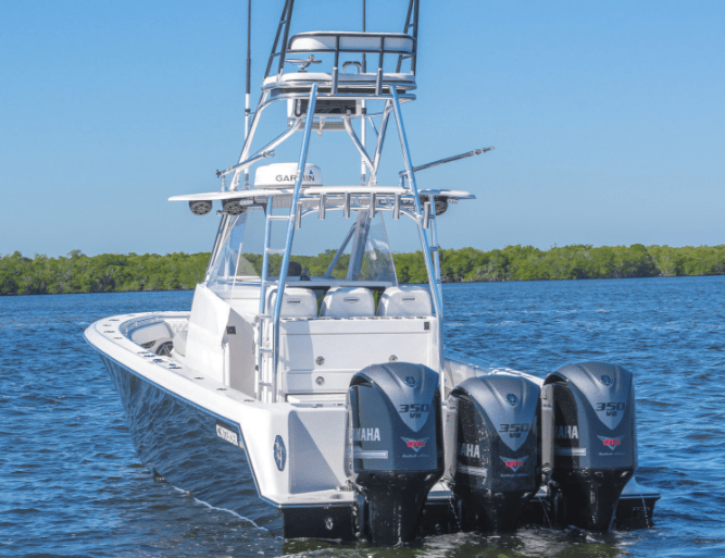 A white powerboat with three Yamaha 350 engines is stationary on a body of water, with a background of green trees.