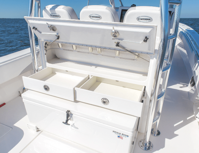 Open storage compartments and drawers on a white boat with labeled "Contender" chairs in the background, set against a backdrop of open water.
