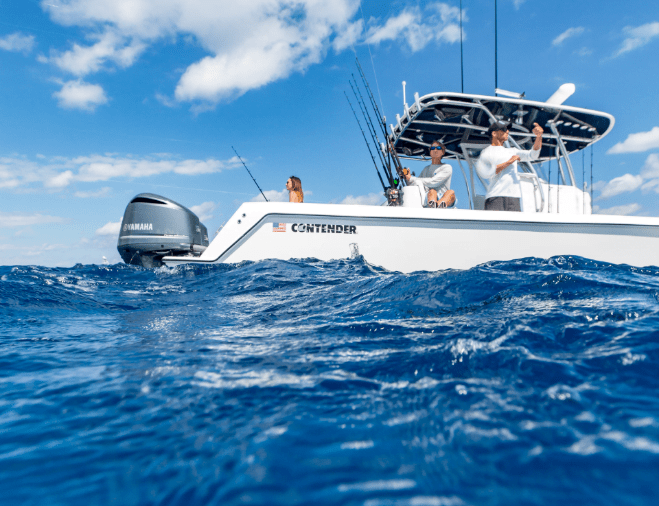 A motorized fishing boat with multiple people onboard is seen on a calm, deep blue ocean with a partly cloudy sky. The boat has several fishing rods and is named "Contender.