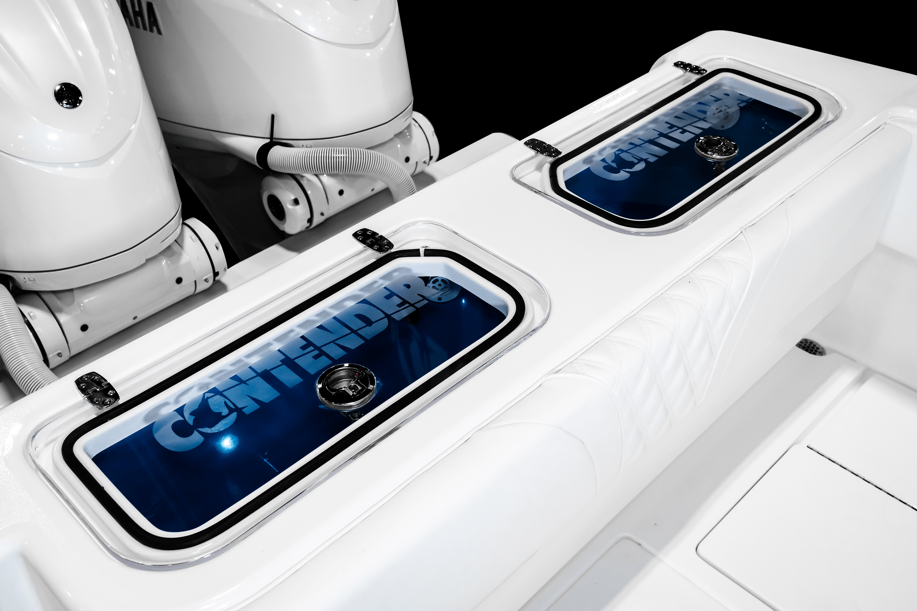 Close-up of the live well hatches with the "Contender" logo on a white boat, showing two Yamaha outboard motors in the background.