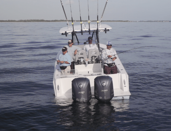 Four people fishing from a boat in calm, open water, with several fishing rods mounted at the back.
