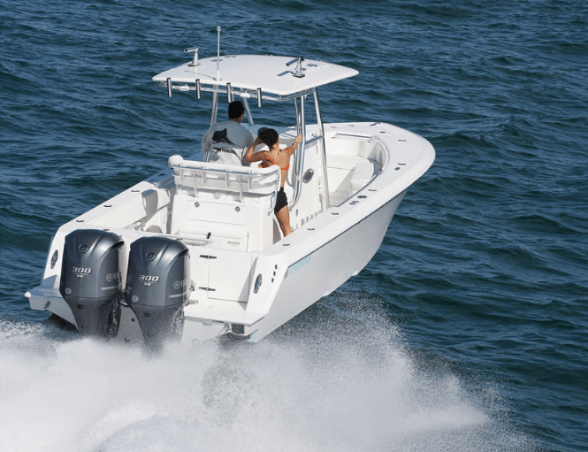 A small white motorboat with two outboard engines moving quickly on the open water, with two people on board wearing life jackets.
