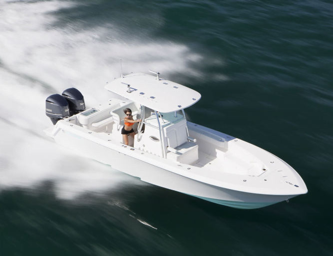 A person steers a white motorboat with twin outboard engines speeding across the water.