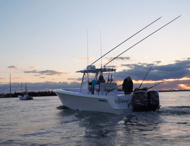 A boat named "Dive" with fishing rods and three people on board moves across a body of water at sunset.