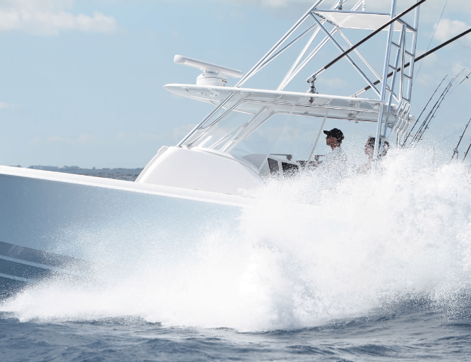 A white motorboat is moving at high speed on the water with two people visible on board; water splashes up in front of the boat.