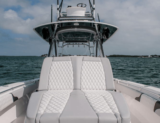 View from a boat's deck featuring a padded lounge seating area, looking toward the helm station with two levels, under a partly cloudy sky.