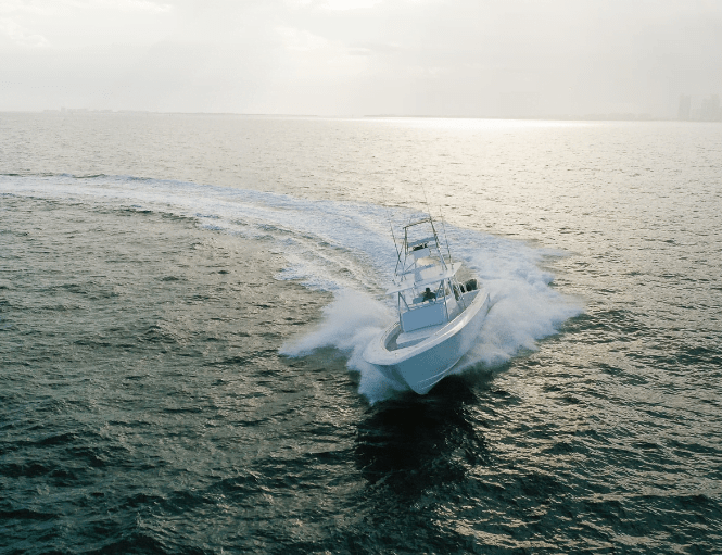 A white speedboat cruises through a large body of water, leaving a trail of frothy waves behind it on a sunny day.