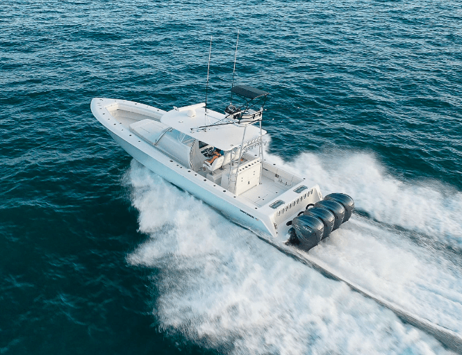 A white speedboat with four engines speeds through the ocean, creating a trail of white foam on the water.