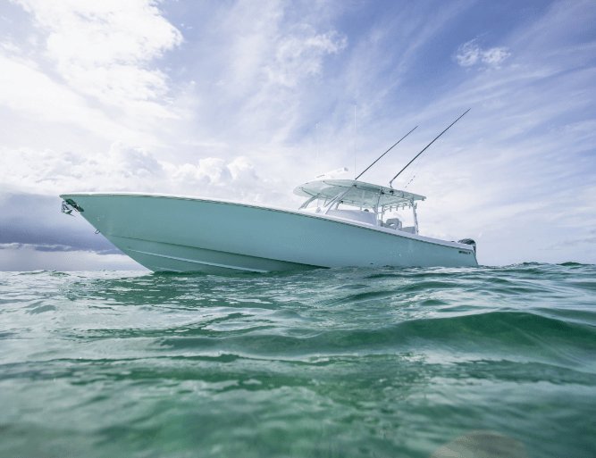 A white motorboat with fishing rods is floating on clear blue water under a partly cloudy sky.