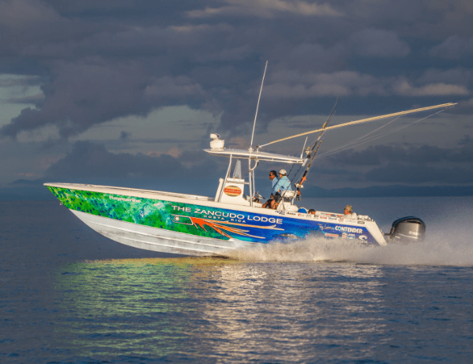 A motorboat with fishing rods on the water, displaying "The Zancudo Lodge" branding on the side, speeding under a cloudy sky.