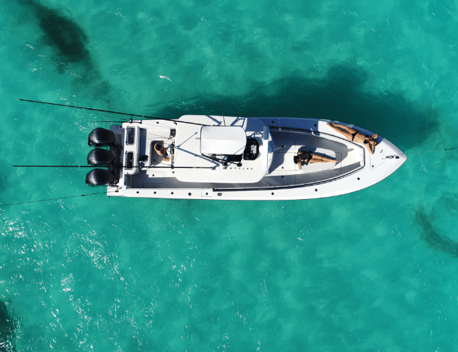 Aerial view of a white motorboat with people on board, floating on clear turquoise water.