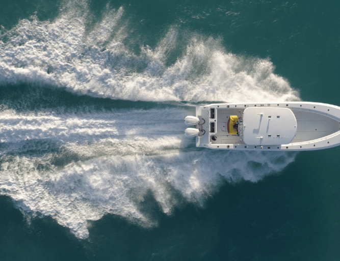 Aerial view of a white motorboat speeding through turquoise water, leaving a wake of foamy waves behind.