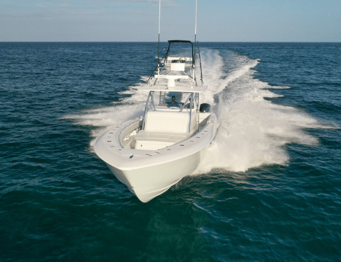 A white speedboat moves swiftly through clear blue ocean water, creating a trail of foam behind it. Two antennas are visible on the boat.