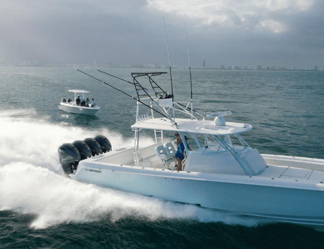 Two motorboats speeding on open water with a city skyline in the background. The larger boat has a person at the helm and multiple rods, while the smaller boat follows behind with three passengers.