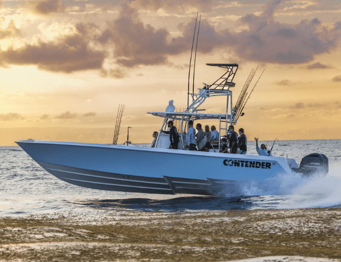 A group of people ride a "Contender" branded boat on the ocean at sunset, with fishing rods visible.