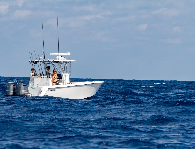 A white powerboat with fishing rods is on the open sea with three people onboard.