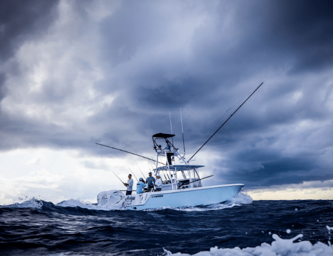 A white fishing boat with multiple passengers navigates through choppy waters under a cloudy, darkening sky.